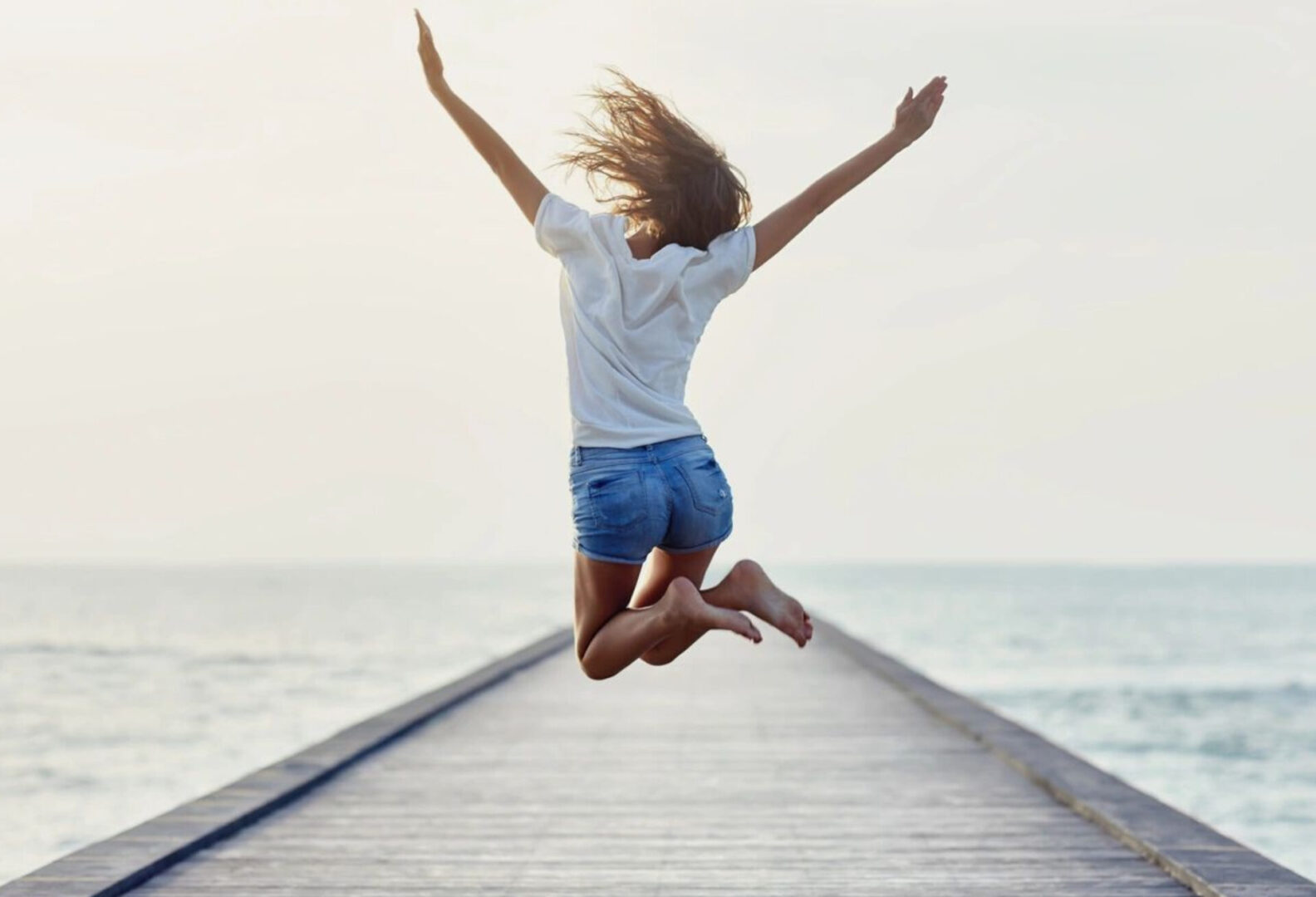 a girl jumping high with excitement near a sea