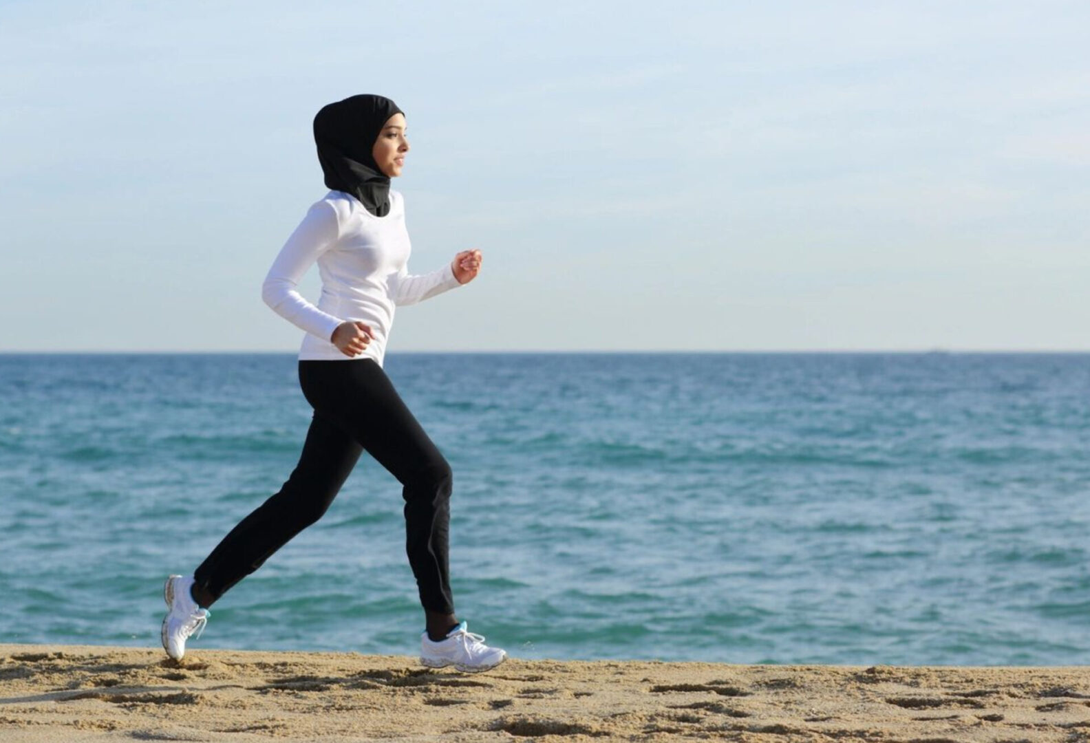 a woman in a white shirt running at a beach